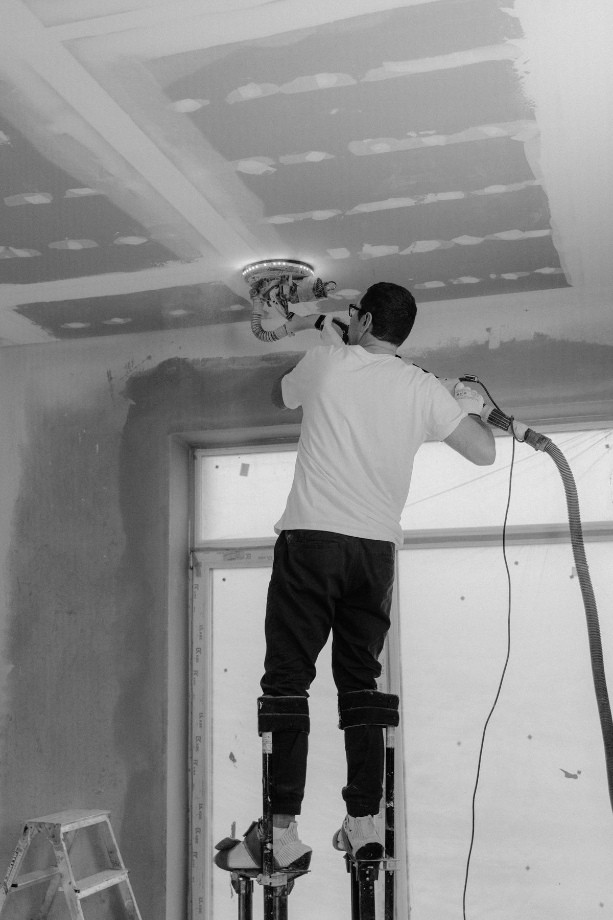 Tradesman on drywall stilts running a sander across a freshly skim-coated ceiling