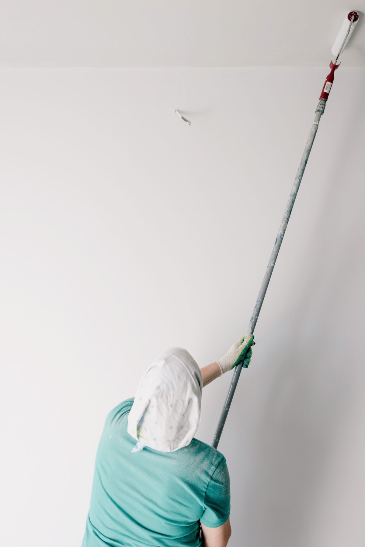 Painter using an extension-pole roller to apply fresh white paint to a smooth ceiling